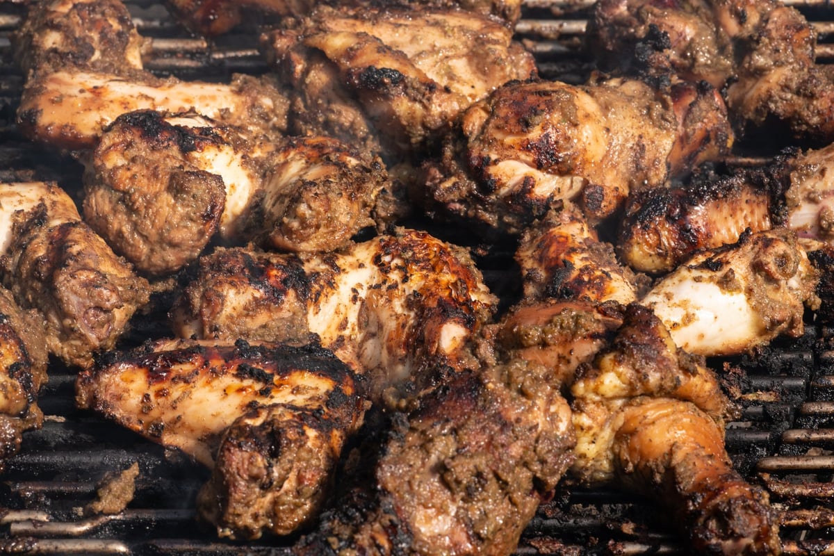 Grilling traditional Jamaican spicy jerk chicken over charcoal fire